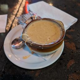 Creamy soup in a bowl on a white saucer with a spoon on a dark stone table