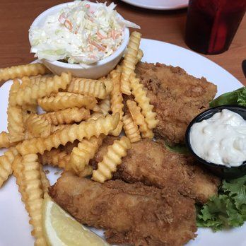 Fried chicken strips with crinkle fries, coleslaw, dipping sauce, and a lemon wedge on a white plate.