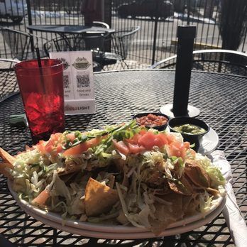 Large platter of tacos on an outdoor patio table with salsa and a red drink