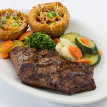 Grilled steak with stuffed potato halves, broccoli, and mixed vegetables on a white plate