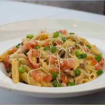 Pasta in a white bowl topped with diced tomatoes, green onions, and grated cheese