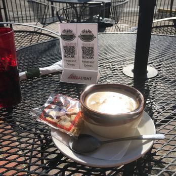 Coffee cup on outdoor café table with pastry, spoon, and drink menu cards in the background