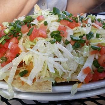 Tostada topped with shredded lettuce, diced tomatoes, onions, and green onions on a white plate