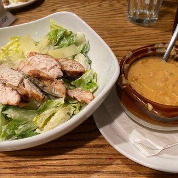 Chicken salad with lettuce and cucumber, served beside a bowl of creamy orange soup on a wooden table