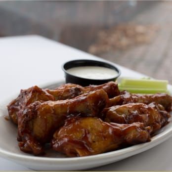 Glazed chicken wings on a white plate with dipping sauce and celery sticks