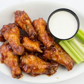 Chicken wings with barbecue sauce and celery sticks on a white plate with a cup of ranch dip