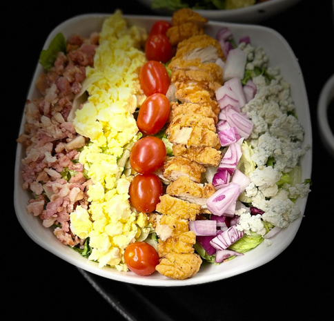 A salad with chicken , eggs , tomatoes , onions and cheese