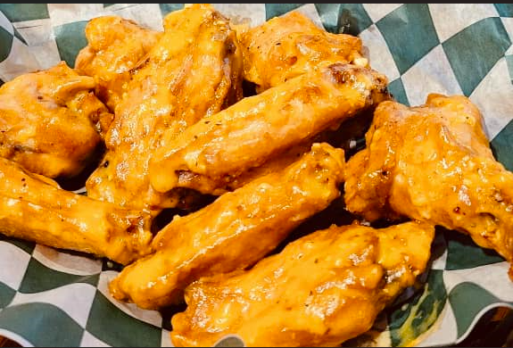 A basket of chicken wings on a checkered paper on a table.