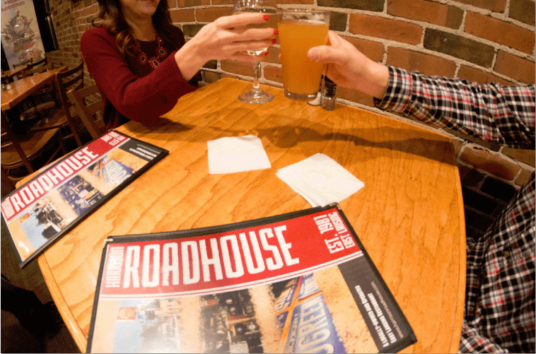 A man and a woman are sitting at a table with a broadhouse menu on it.