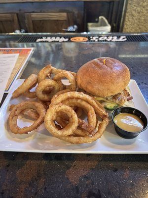 Burger and onion rings on a white plate with dipping sauce on a restaurant table
