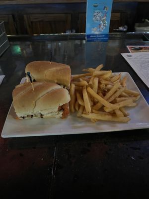 Plate with a sandwich and French fries on a table in a dimly lit restaurant.