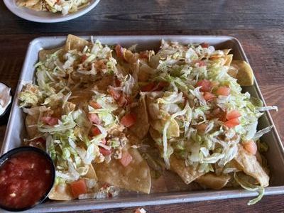 Tray of nachos topped with lettuce, tomatoes, and cheese, served with salsa on a wooden table