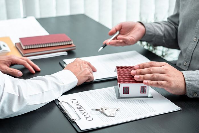 Hands with a Small Model Home, Forms and Another Hand Pointing to the text on the Form  — Residential, Rural & Commercial Property Valuers in Grafton, NSW