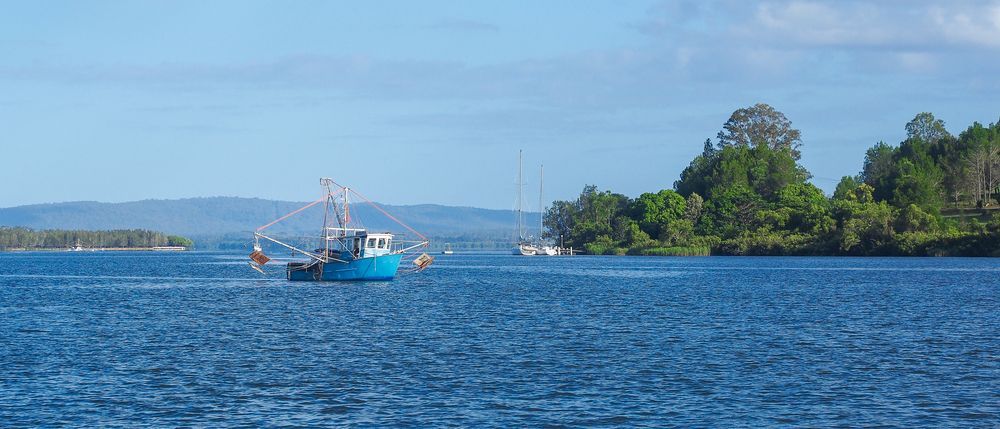 A Blue Boat is Floating on Top of a Large Body of Water — Clarence Property Consultants In Maclean, NSW
