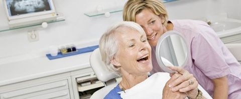 older woman looking at teeth with mirror