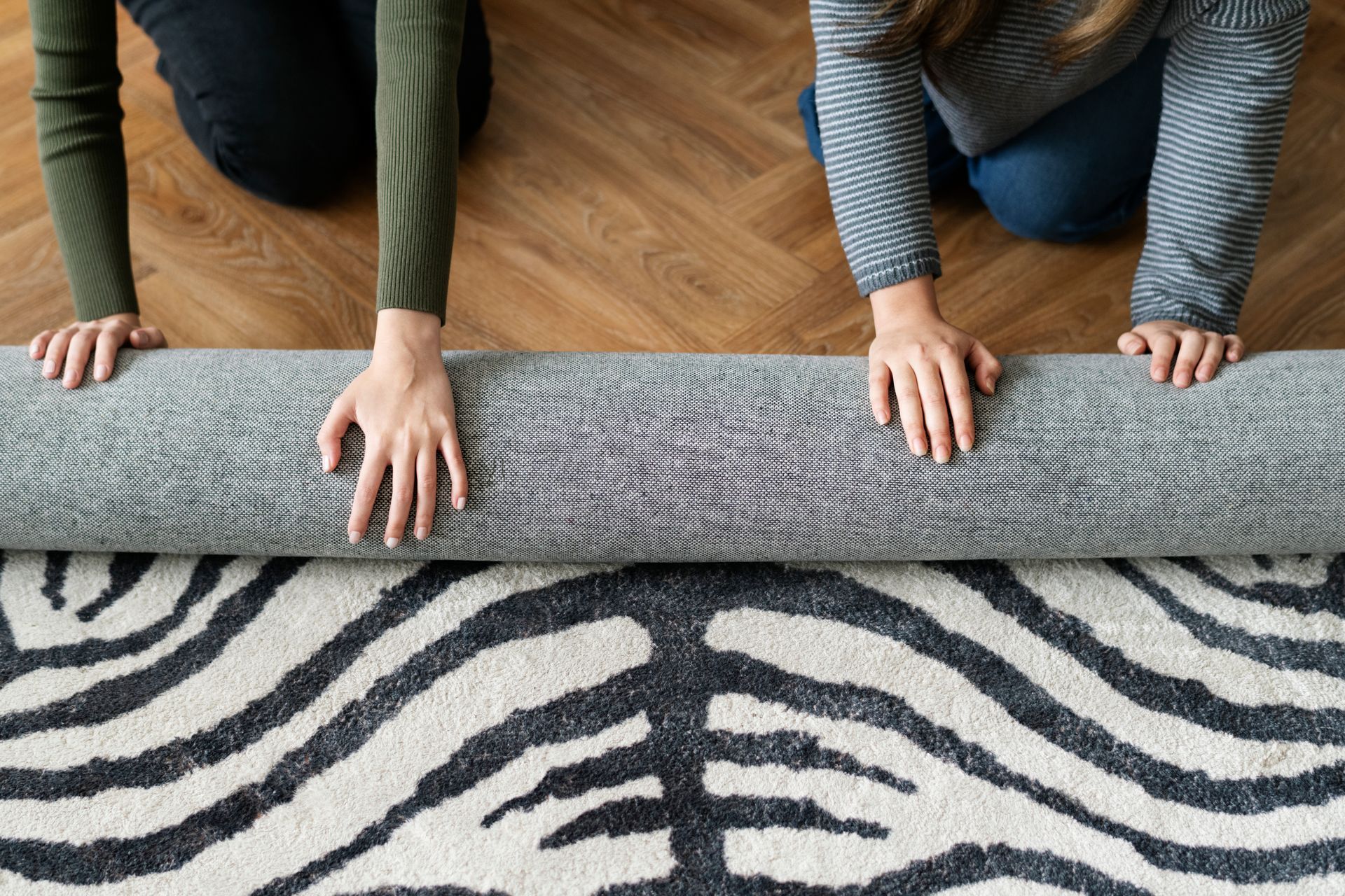 Two women are rolling a rug with a zebra print