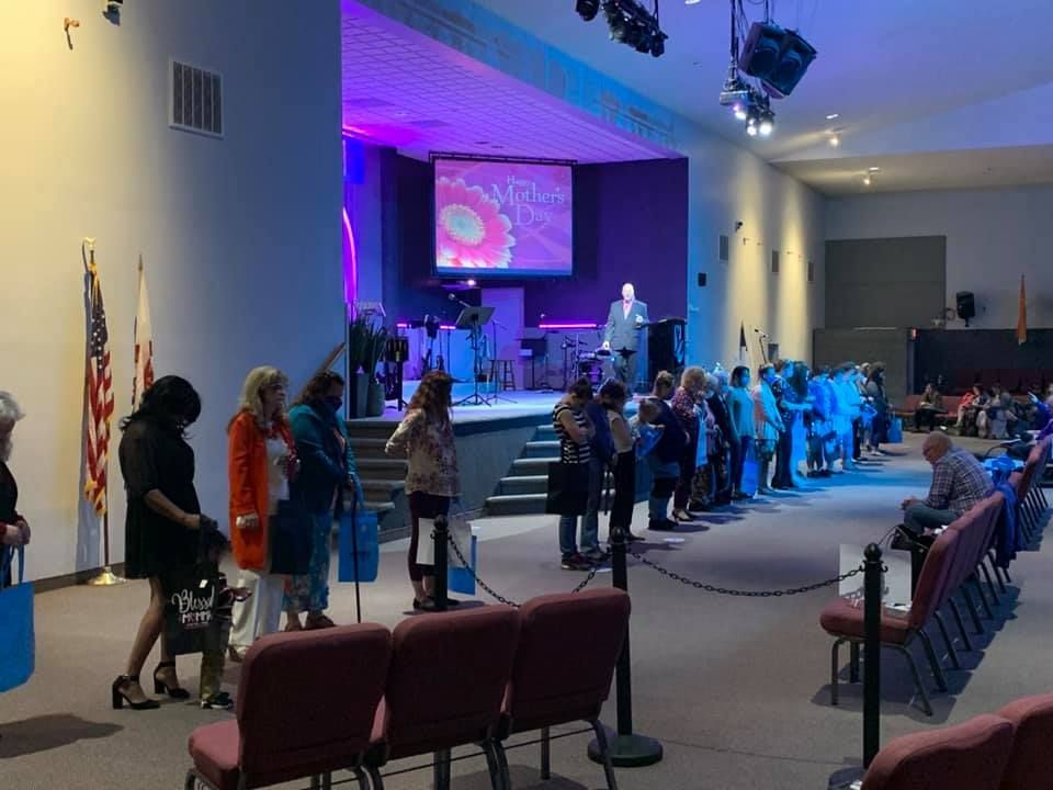 People standing in a church auditorium during a worship service, with purple stage lighting and seated attendees.