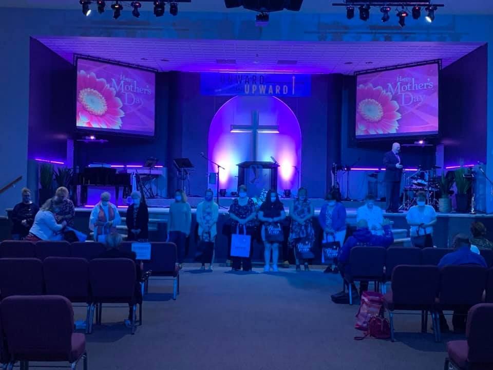 Crowded church sanctuary with purple-blue stage lighting, screens, and people seated and standing during a service