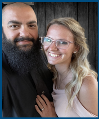 Smiling couple posing closely indoors, with dark wood background and soft lighting.