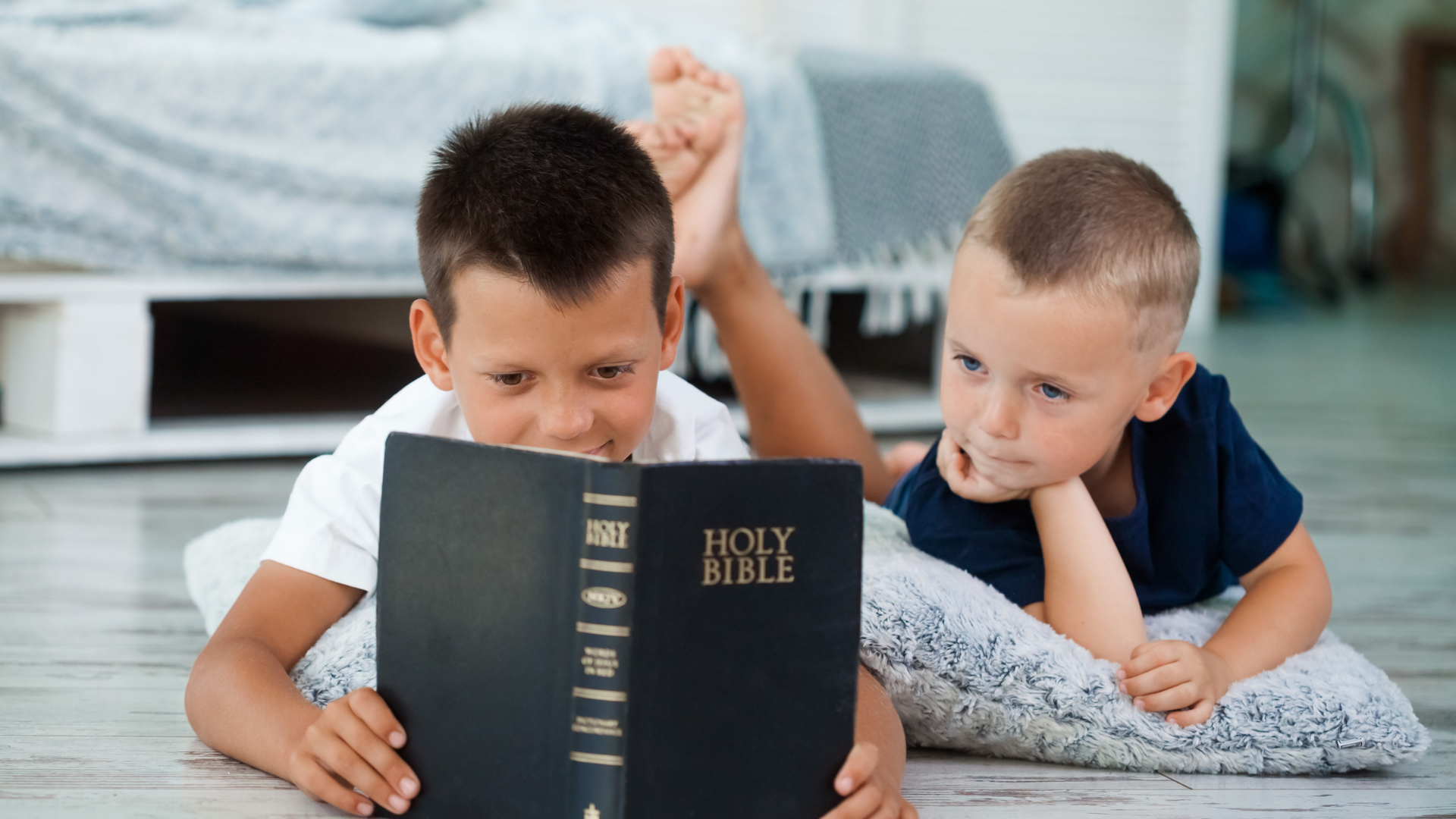Two children lying on a bed, reading a Bible together.