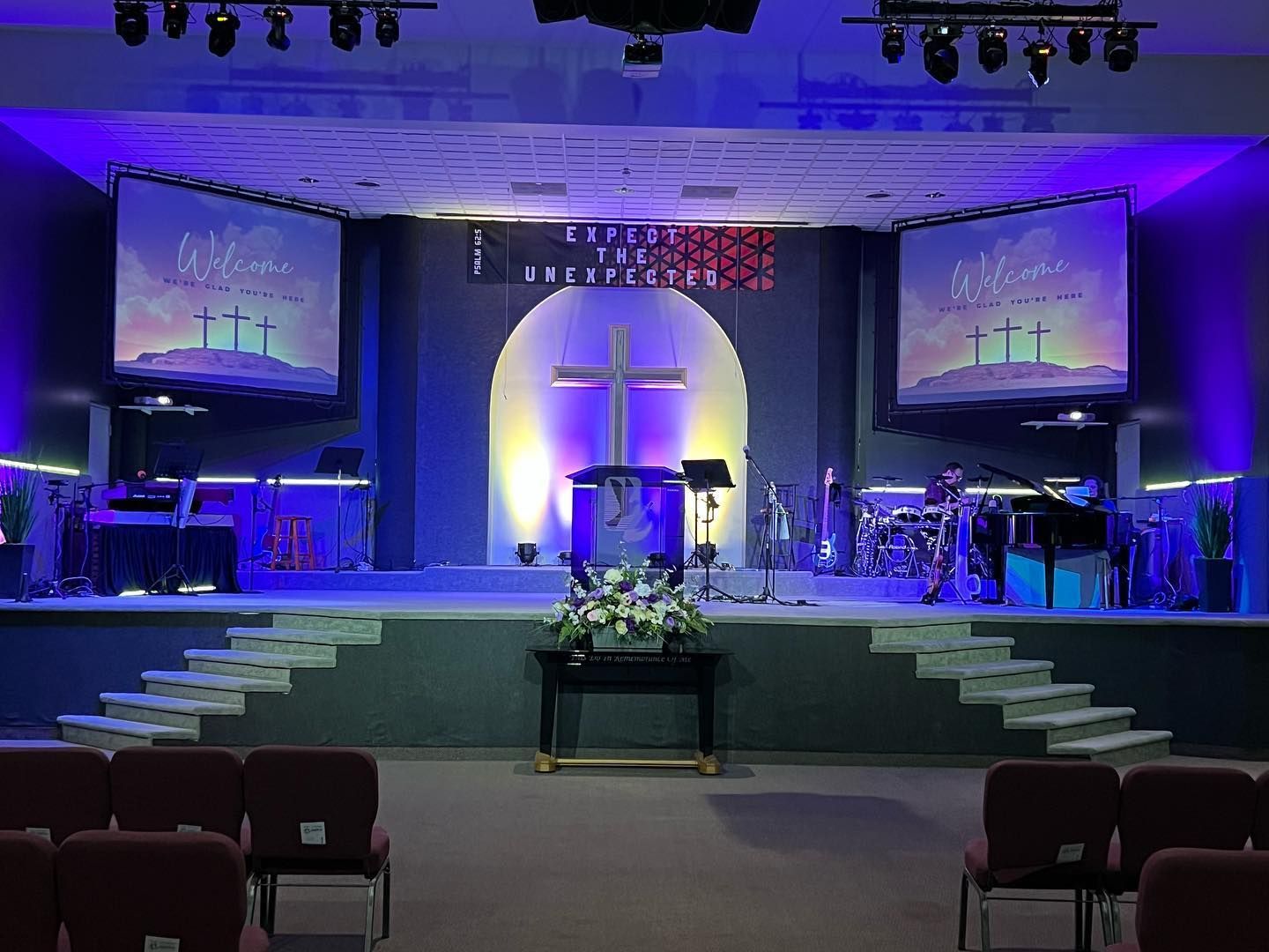 Church stage with illuminated cross, blue-purple lighting, and two projection screens above an empty seating area
