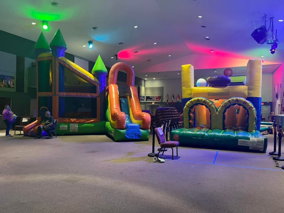 Indoor inflatable play area with colorful bounce structures, slides, and neon lights; mostly empty.