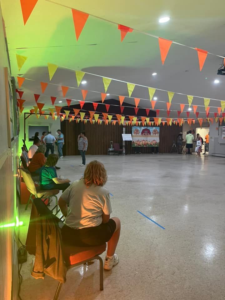 Decorated hall with orange bunting, a small seated crowd, and a stage at the far end
