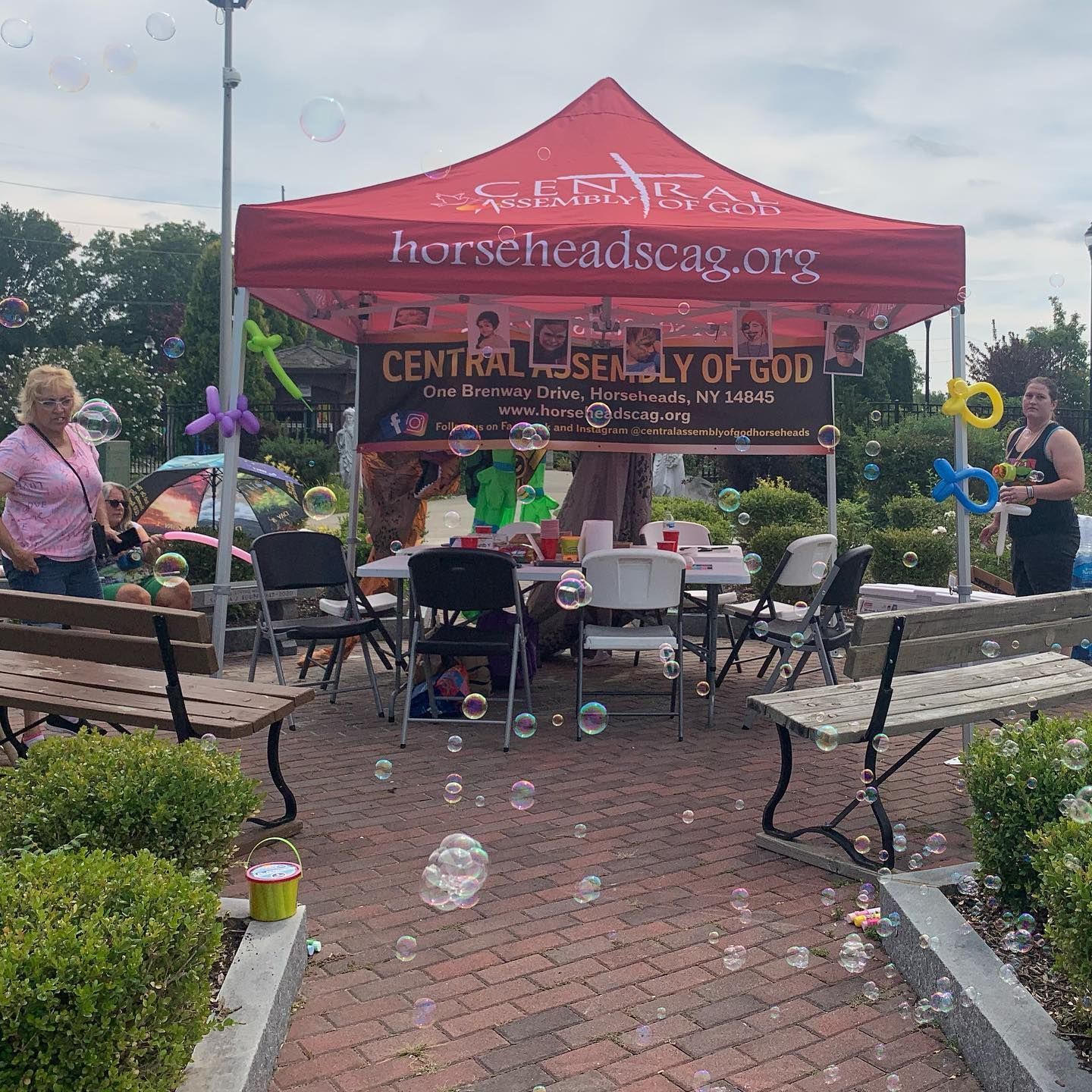 Red canopy tent at a park event with benches, bubbles, and people gathered around tables.