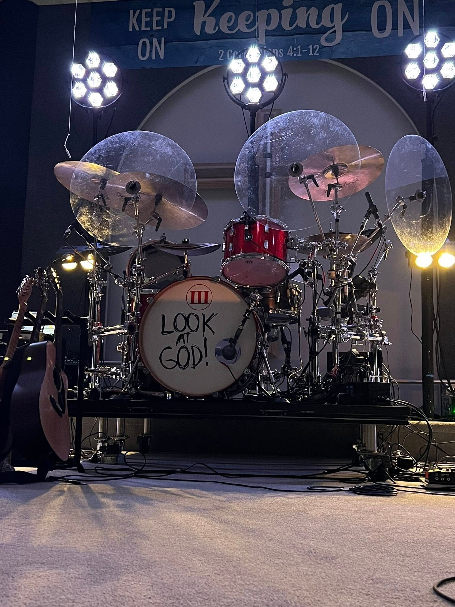 Drum kit on stage with bright lights and “Keeping On” and “Look to God!” signs