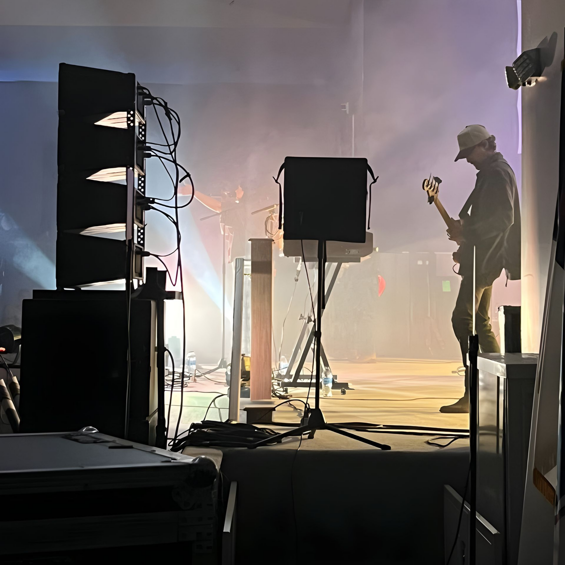 Silhouetted guitarist on a hazy stage with bright backlights and audio equipment in the foreground
