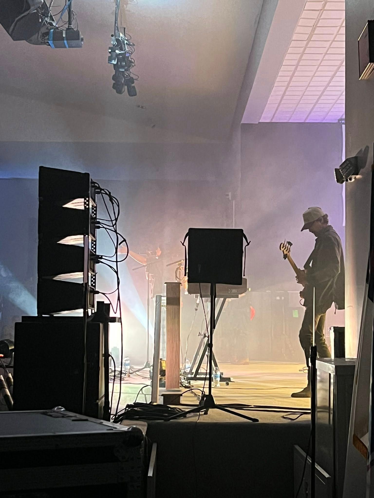 Concert stage with two musicians, speakers, and haze lighting from backstage view