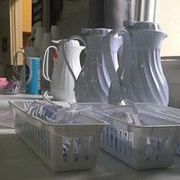 White pitchers and plastic baskets lined up on a kitchen counter near a window.