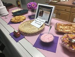 Table with buffet dishes, flowers, and a framed sign on purple placemats indoors
