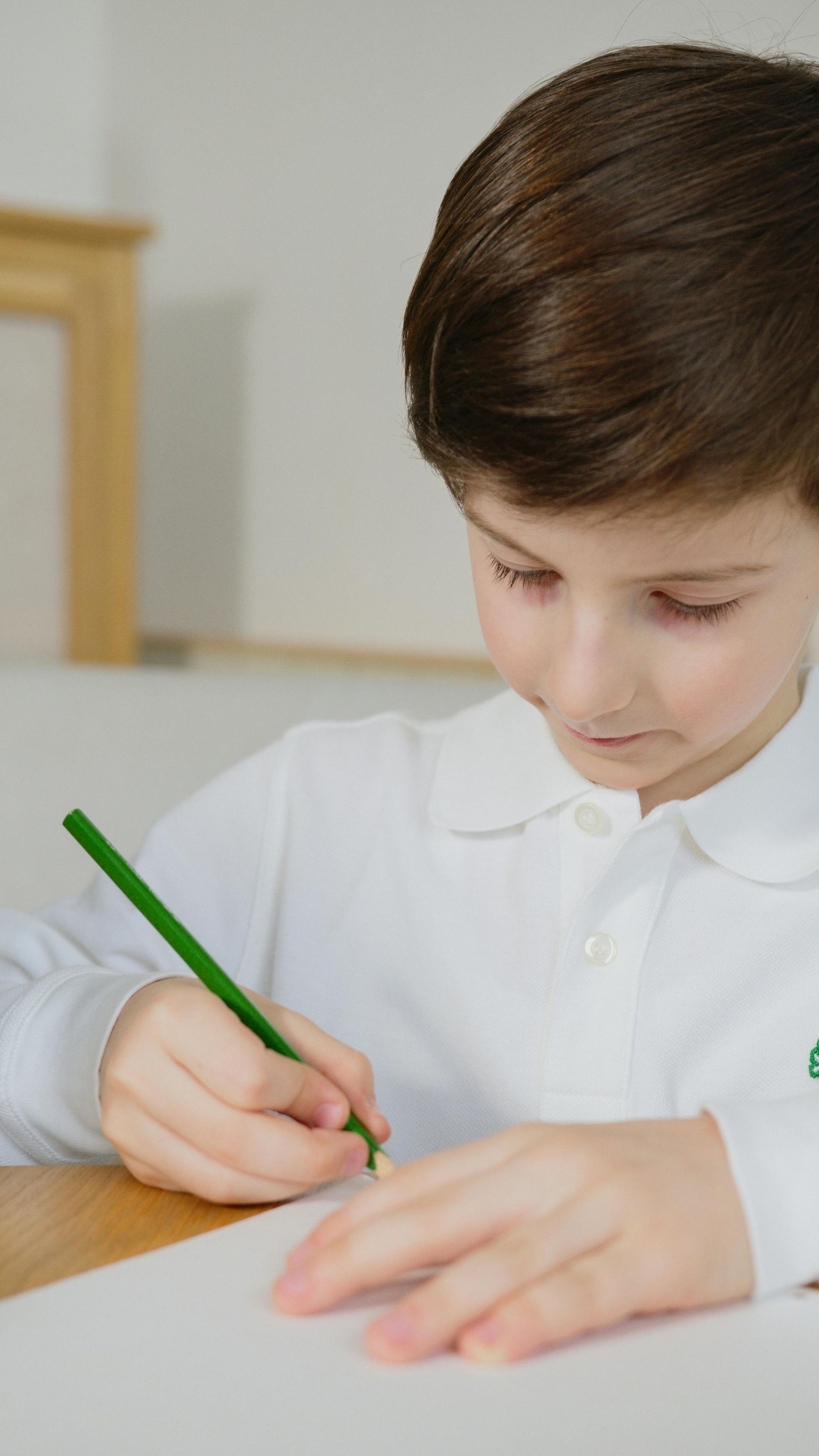 Child writing with a green pencil on paper at a table