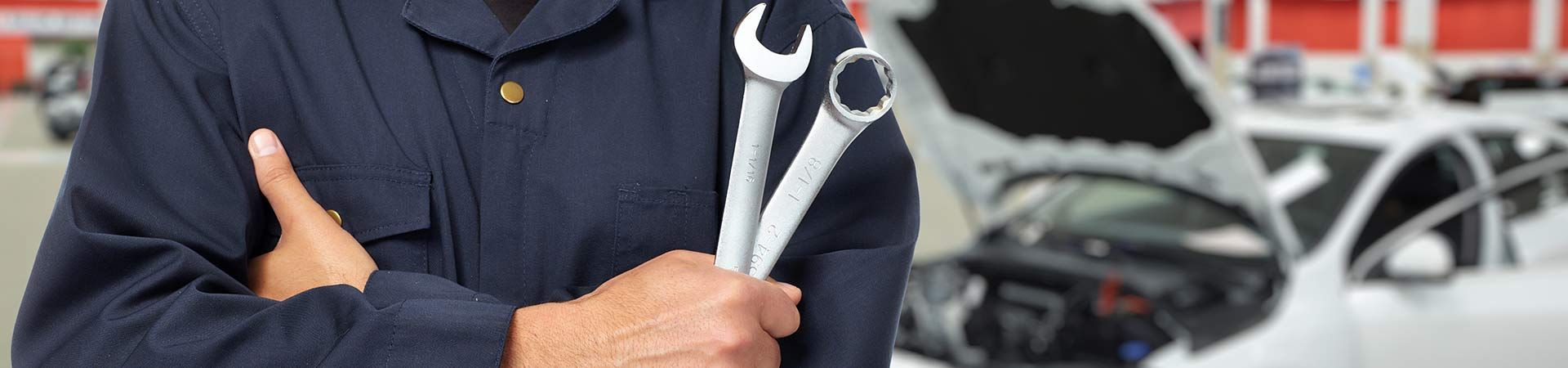 A mechanic is holding a wrench in front of a car with the hood open - A Street Automotive