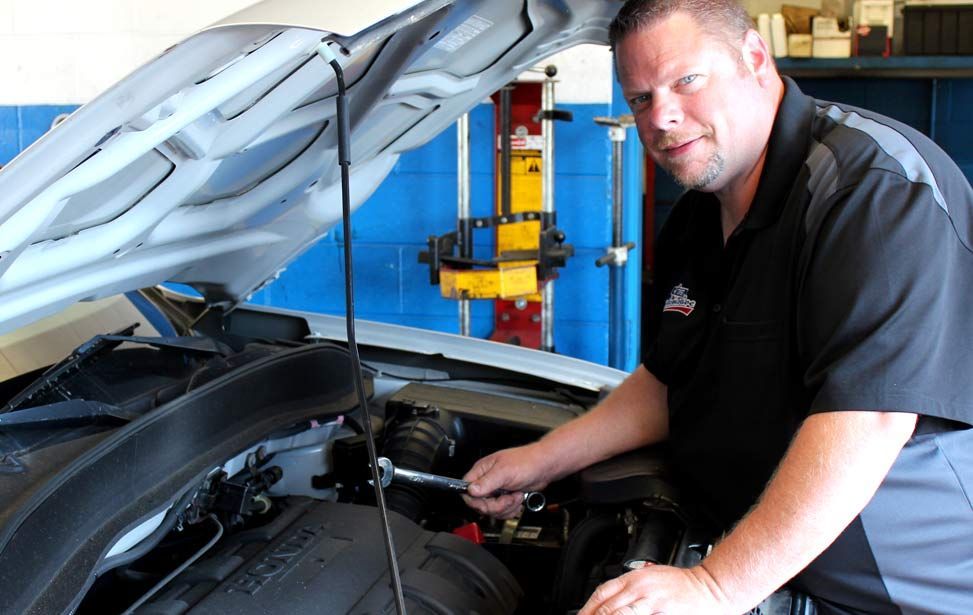 A man is working under the hood of a car - A Street Automotive