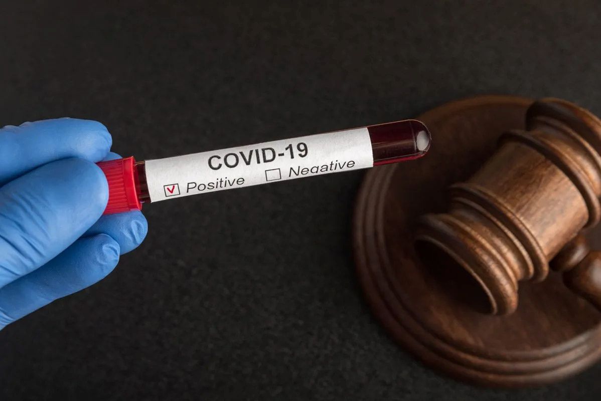 A Hand in a Blue Glove Holds a COVID-19 Test Tube Near a Wooden Gavel — Bradley Solicitors in Larrakeyah, NT