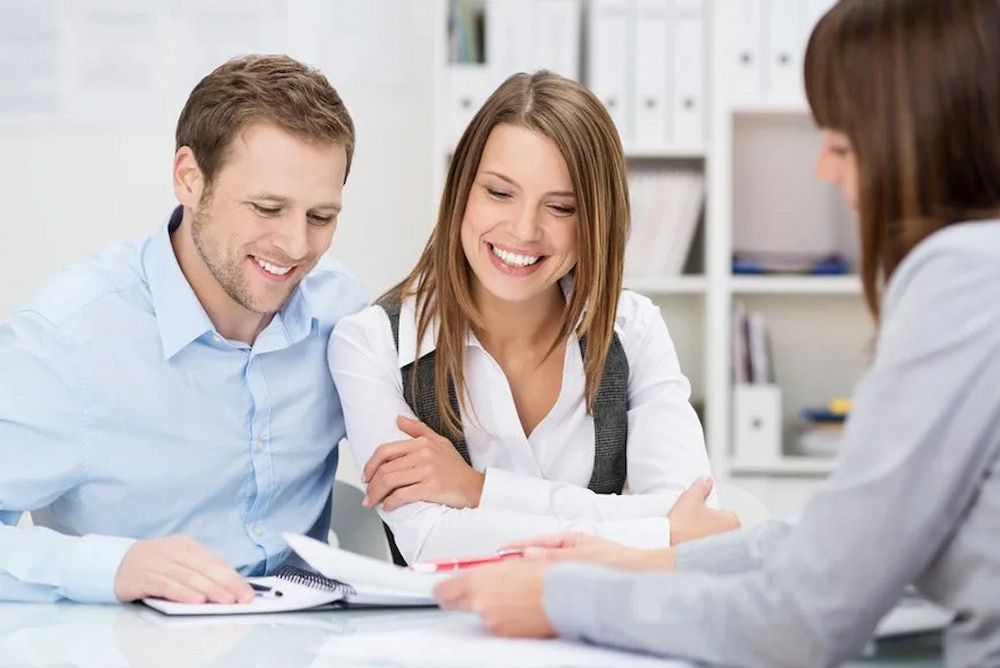 Couple Smiling, Reviewing Documents With a Professional in an Office — Bradley Solicitors in Larrakeyah, NT