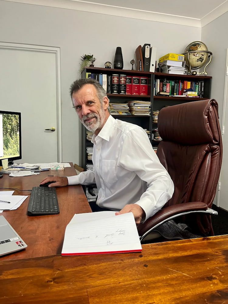 Man in White Shirt Sits at a Desk, Looking at the Camera — Bradley Solicitors in Larrakeyah, NT