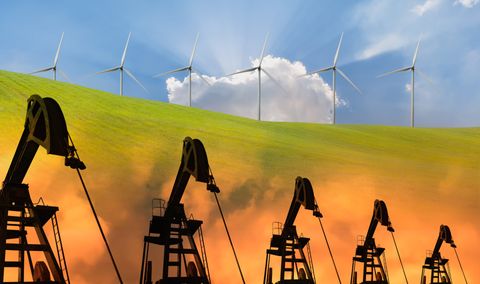 line of wind turbines with blue sky and green grass above and a line of oil drilling rigs with orange smoke below