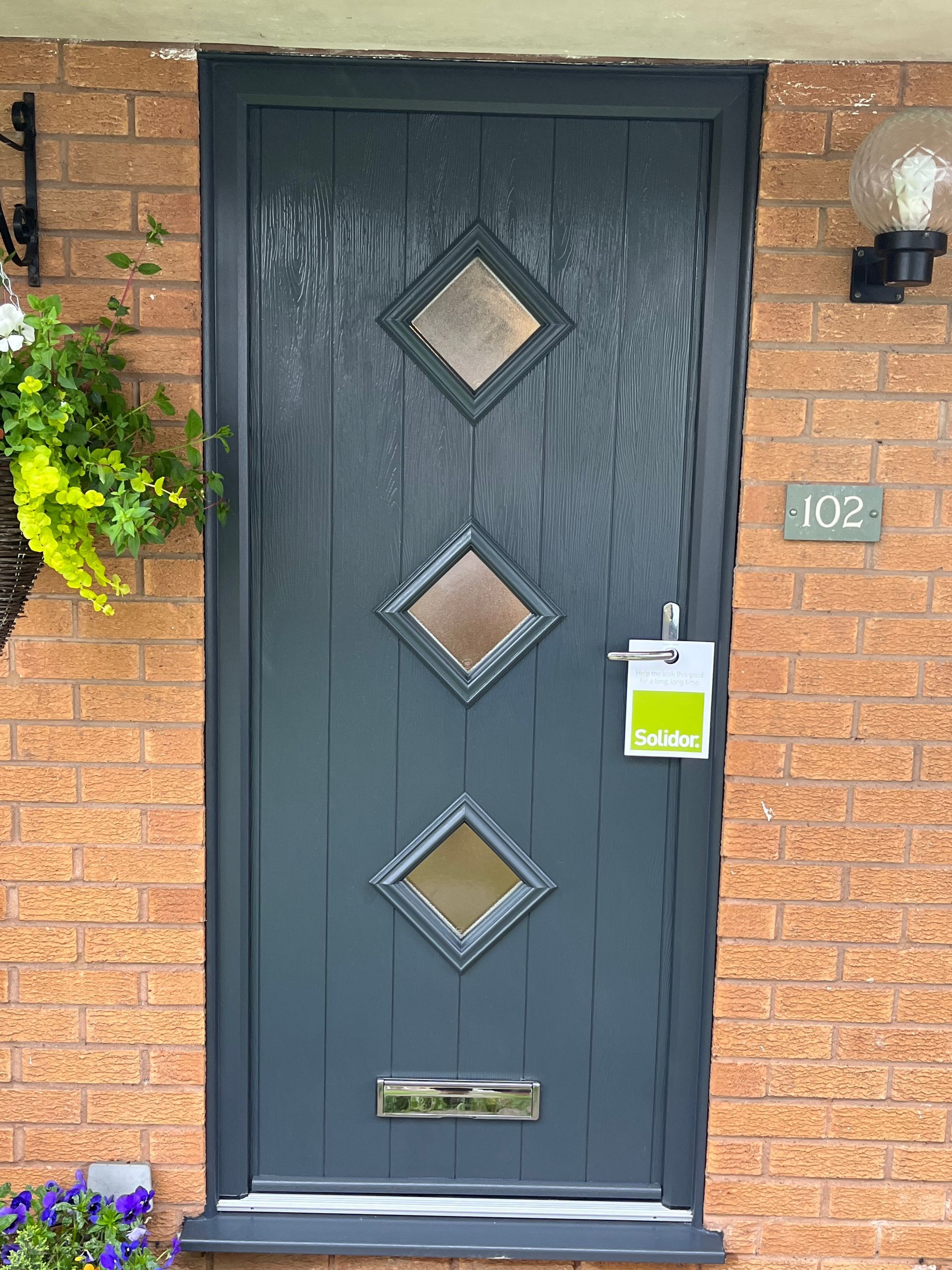 A black door with three square windows is on a brick wall.