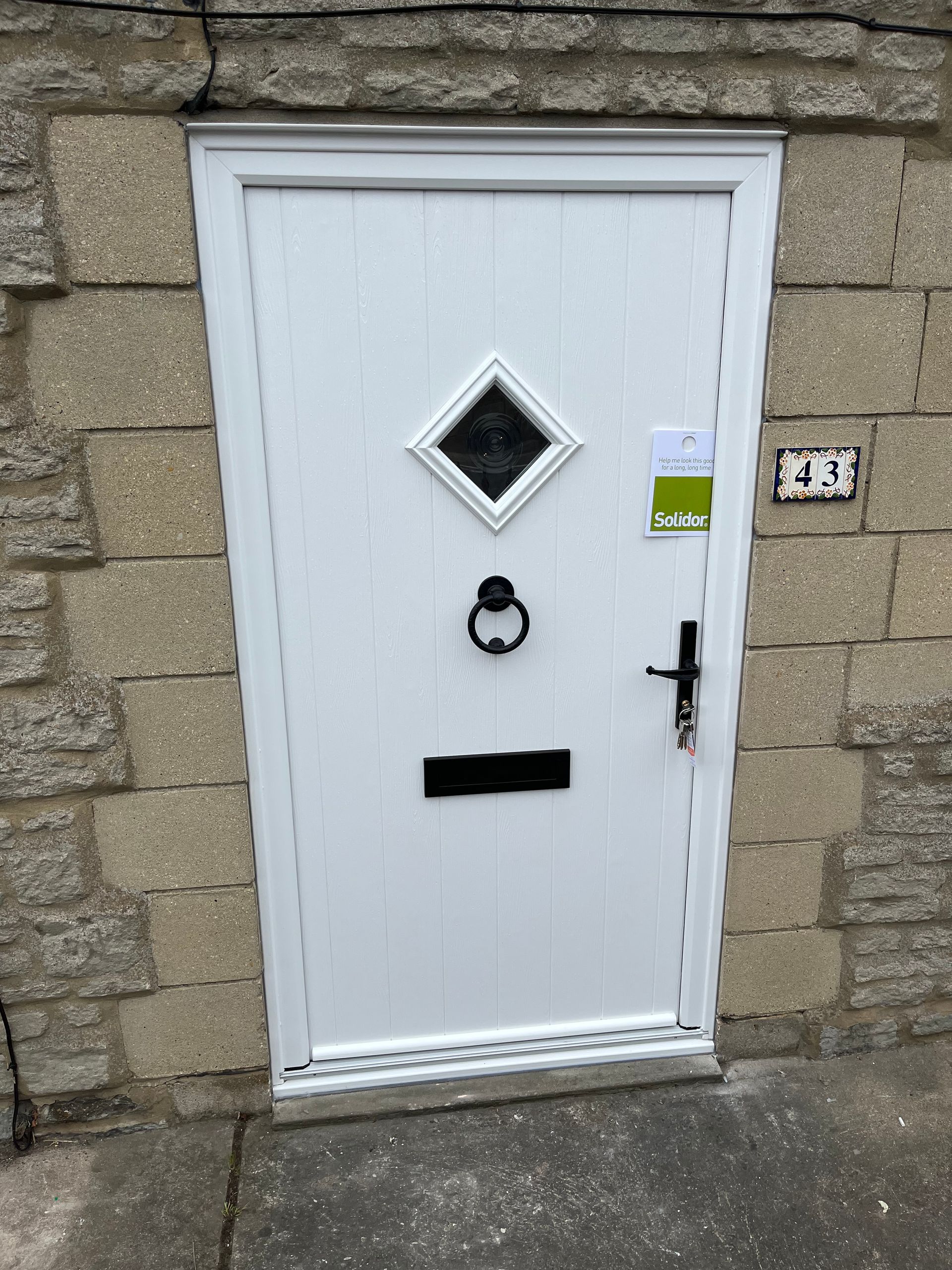 A white door with a diamond design on it is against a brick wall.