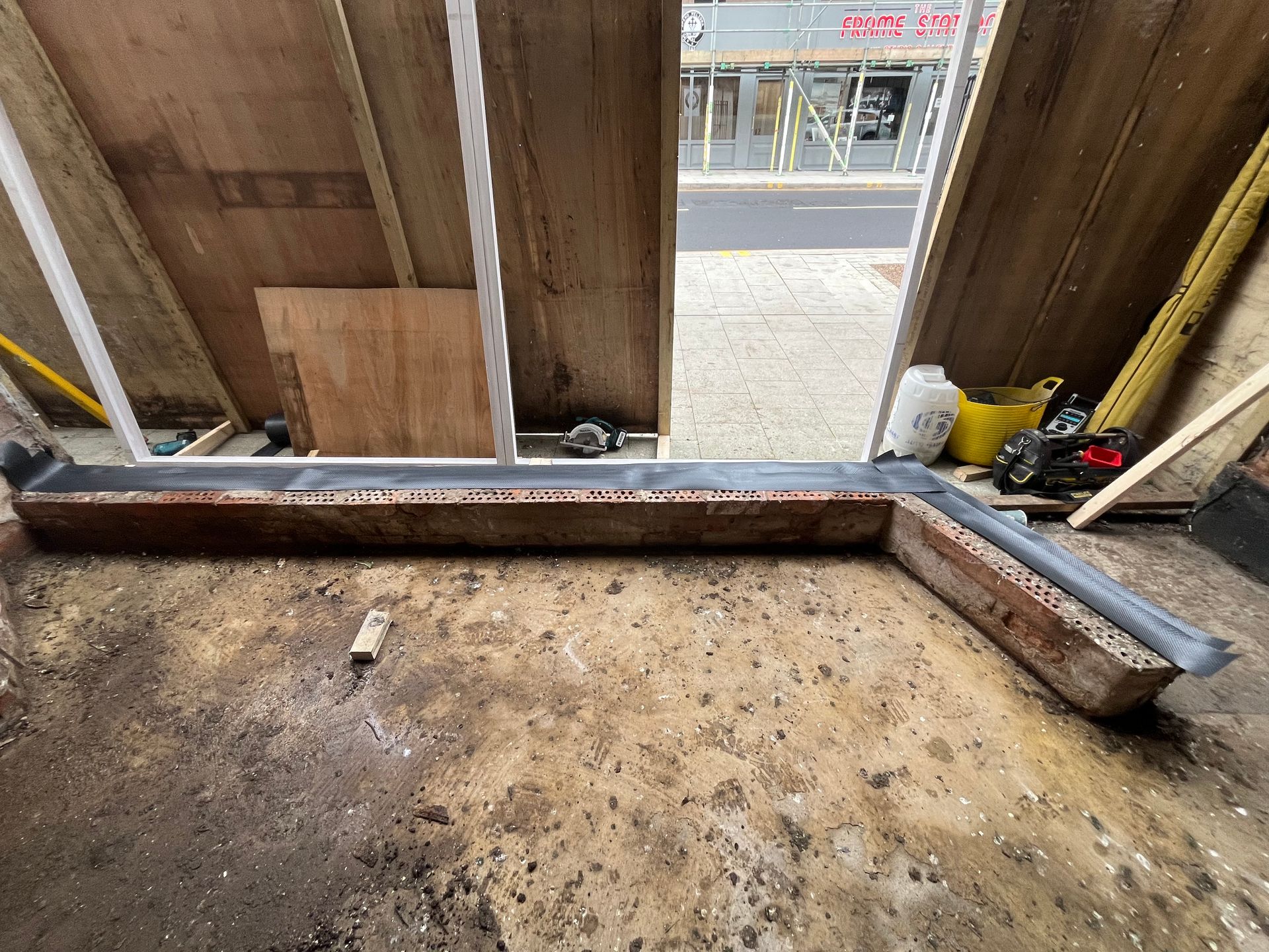 A dirty room with a window and a drain on the floor.