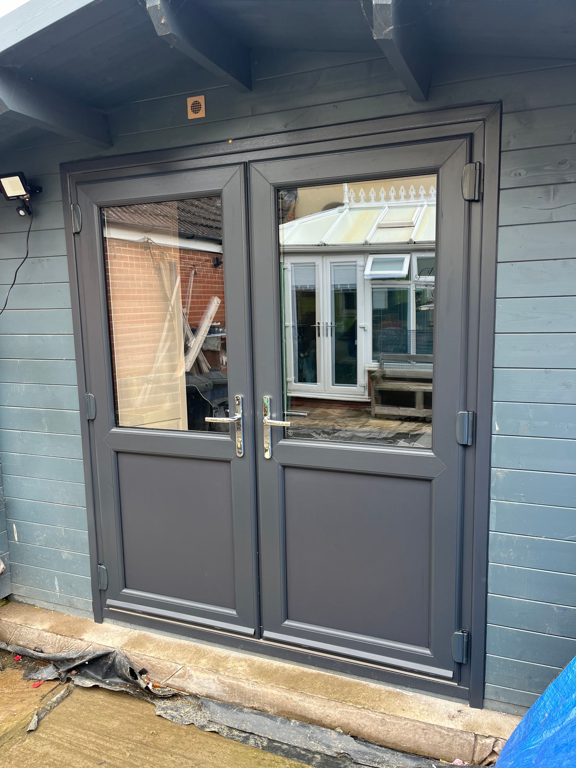 A pair of black double doors with a window on the side of a building.