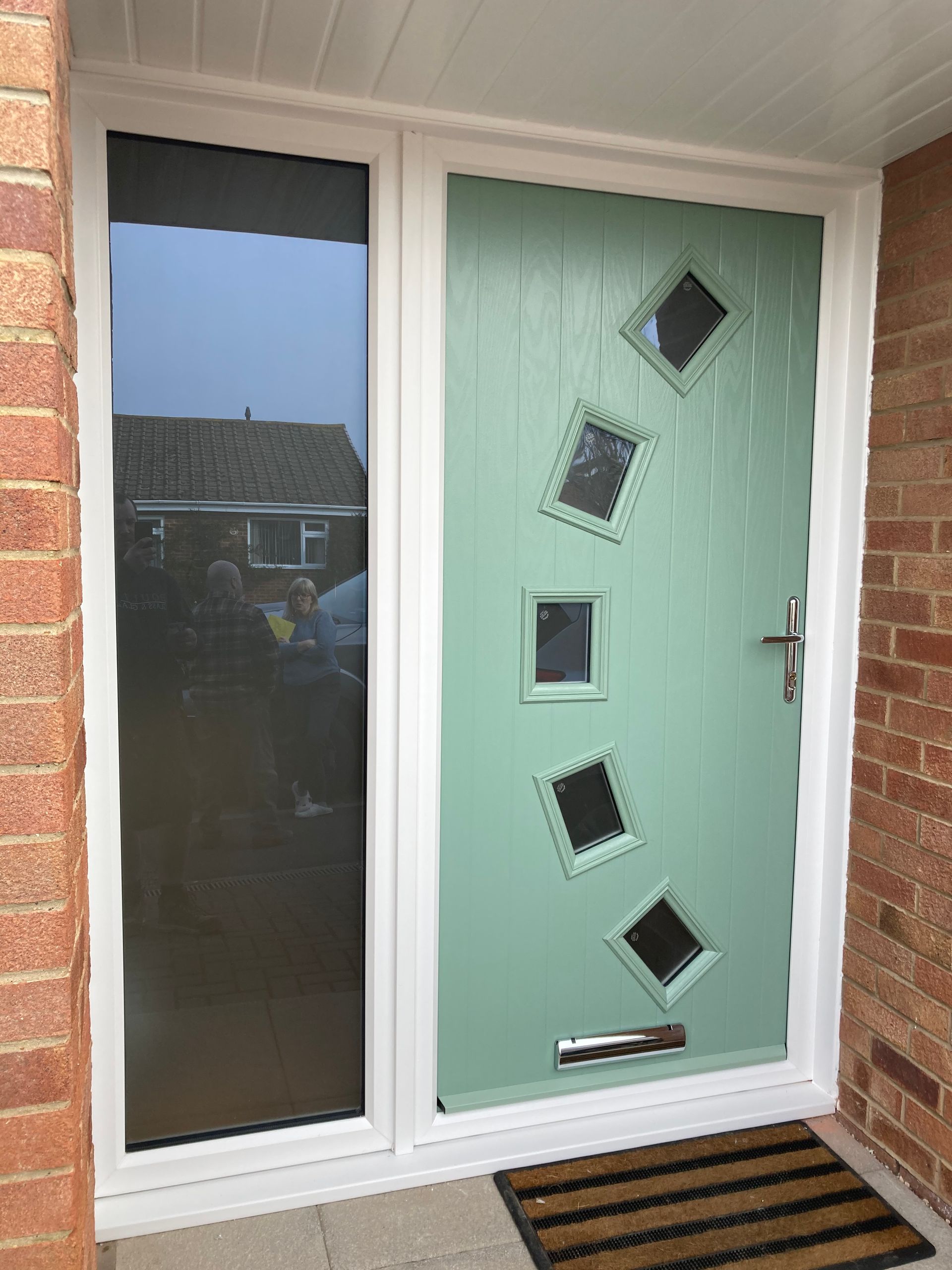 A green door with squares on it is on a brick wall.