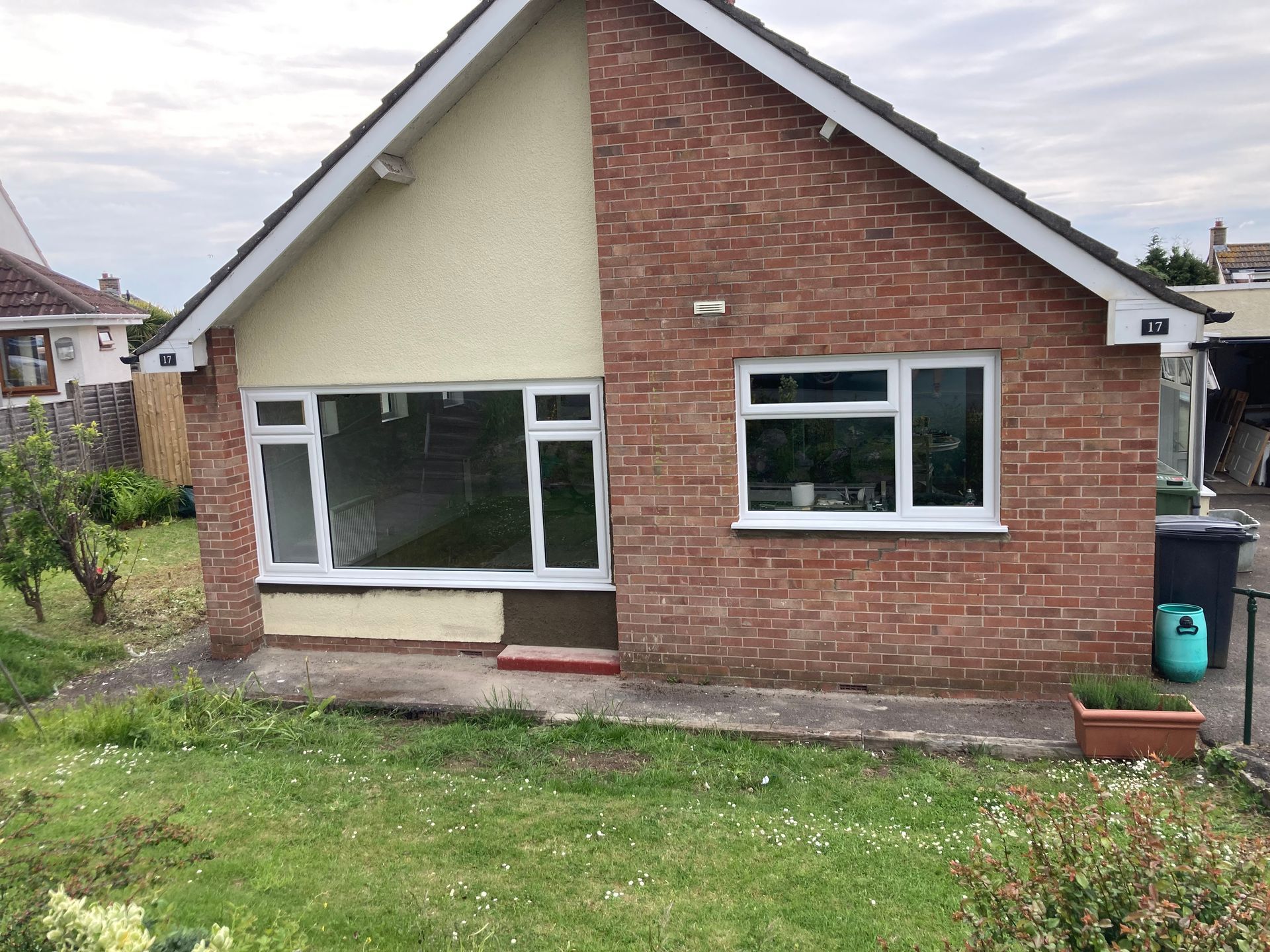 A small brick house with a white roof is sitting in the middle of a lush green yard.
