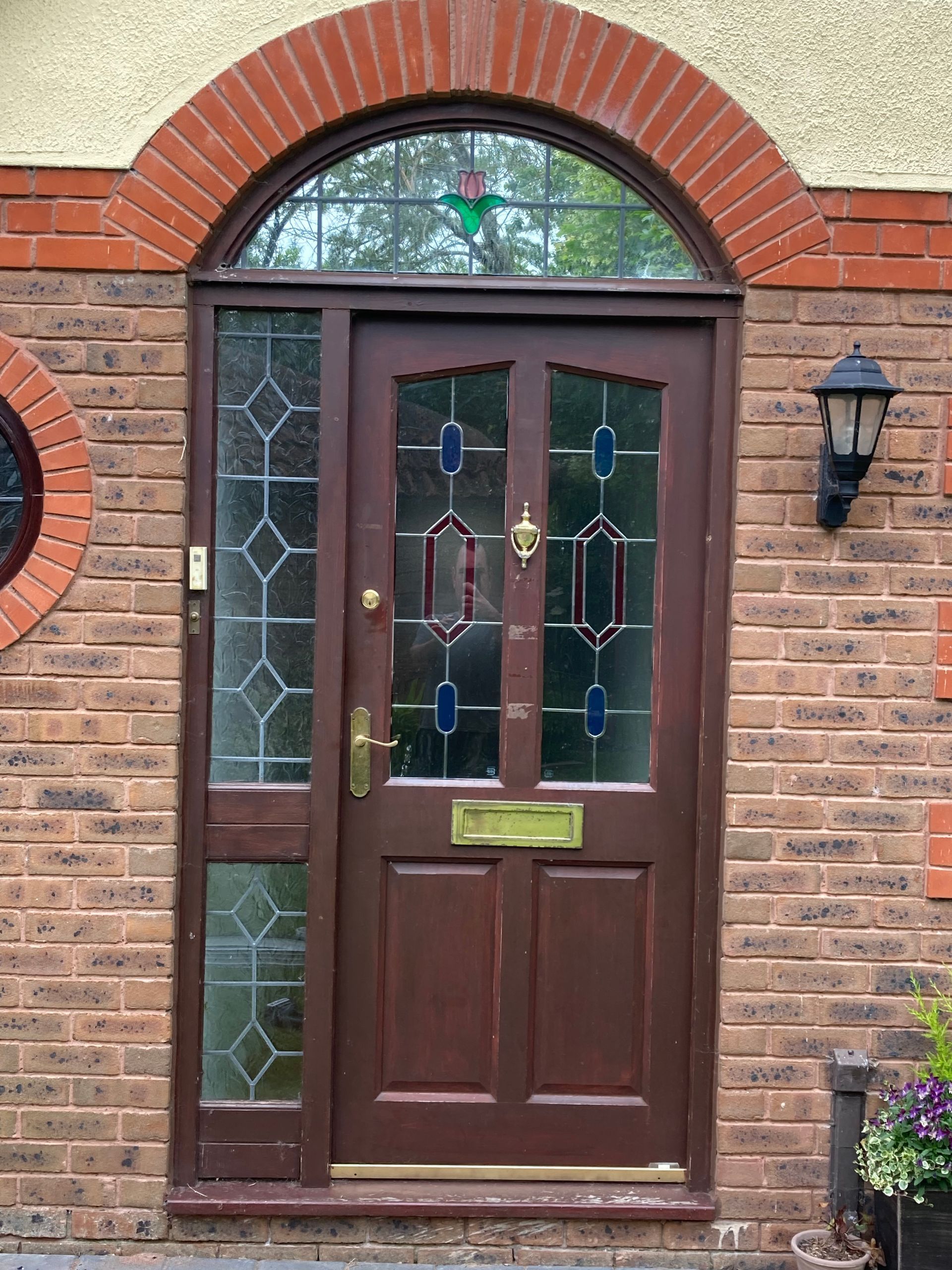 A brown door with a stained glass window is on a brick building.