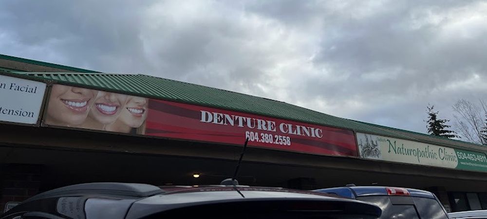 Exterior of a Denture Clinic with a red banner. Above it, there is a cloudy sky and the roof of the building is green.