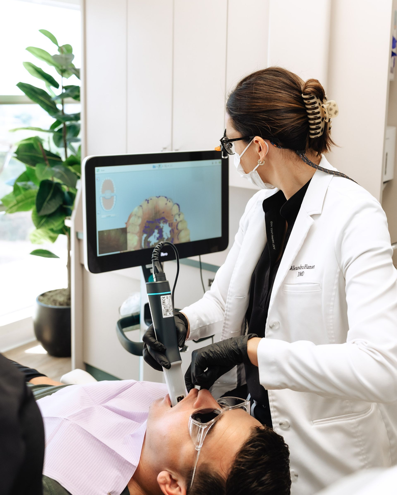 Dentist pointing at teeth scan on screen, explaining to patient reclining in chair, dental office.