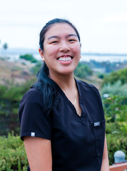 Smiling Asian woman in black scrubs poses outdoors.
